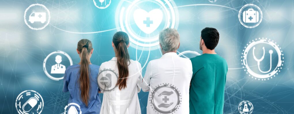 A team of doctors and nurses standing with their backs to the camera, looking at a complex, blue digital display with interconnecting health and medical icons like a heart, syringe, and ambulance, representing advanced healthcare technology and network.
